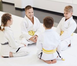 Group of children sitting on the floor together and talking to each other before sport training in karate in the gym