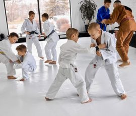 Little boys, children in white kimono training judo, jiu-jitsu sport activity indoors with professional coach. Concept of martial arts, combat sport, sport education, childhood